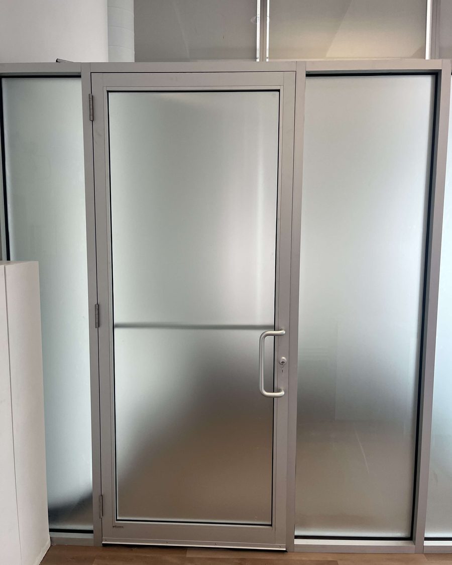 A clear anodized aluminum door with a frosted glass lite and a D-pull handle, between frosted glass sidelites in an office partition