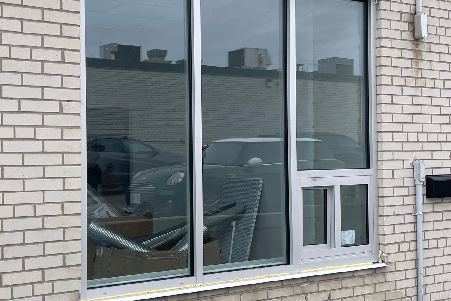 A clear anodized aluminum commercial window in a pale brick wall — two tall fixed lites and a third section with a small sliding vent below its fixed glass