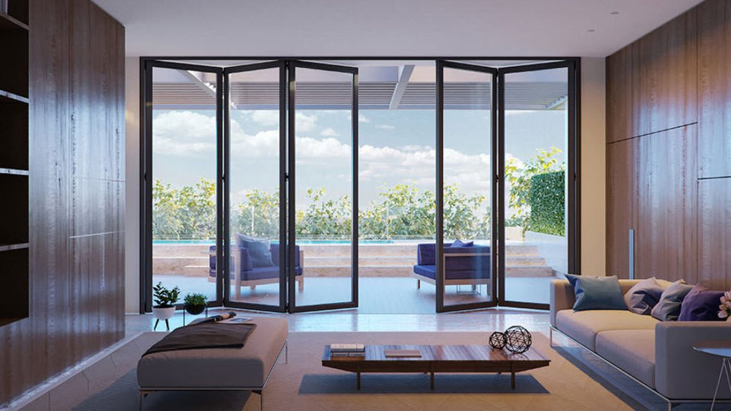 A living room with a dark-framed bifold glass door system across the full width of the back wall, its panels partly folded back at each side, a sofa and low table in front and a pool terrace beyond