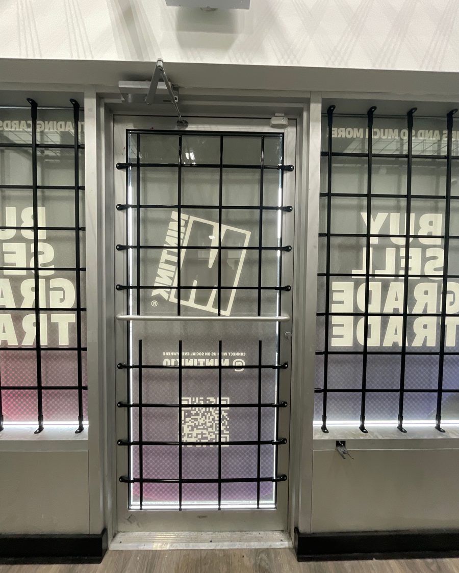 Black steel bars fixed over the glass of an aluminum storefront door and the lites on either side of it, inside a retail unit