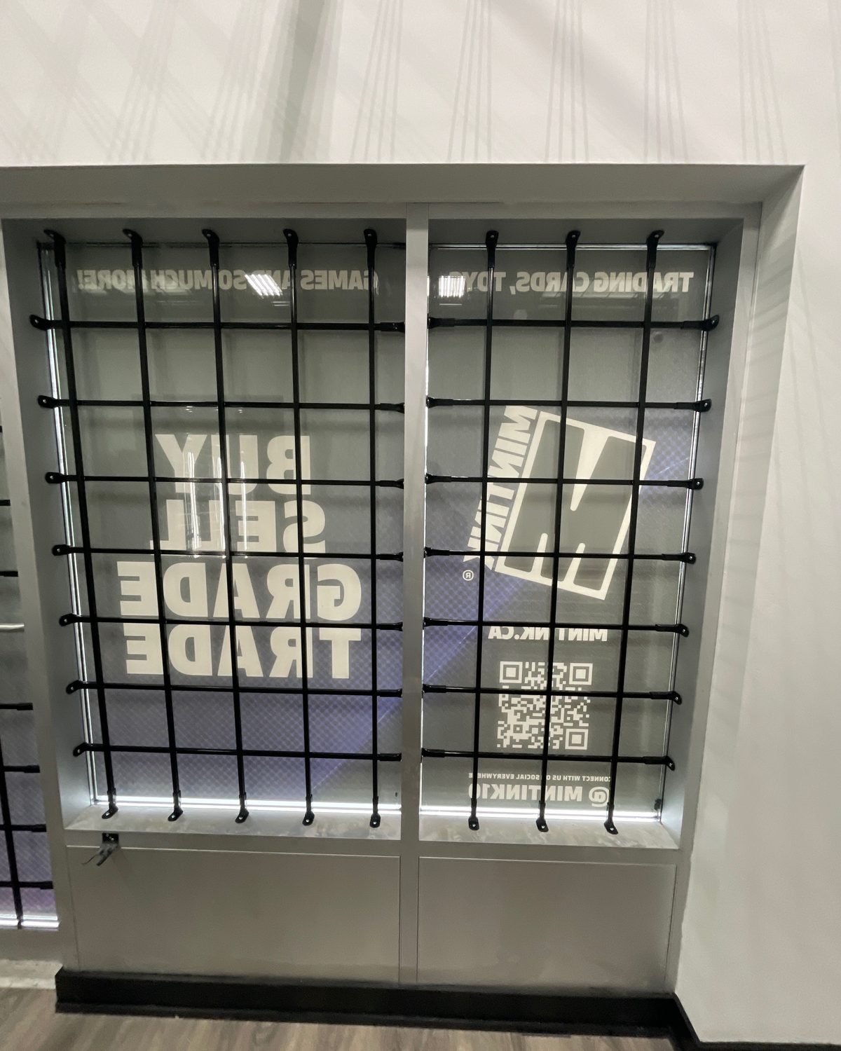 Black steel security bars fixed over two tall storefront lites inside a retail unit, the vinyl graphics on the glass visible behind the bars
