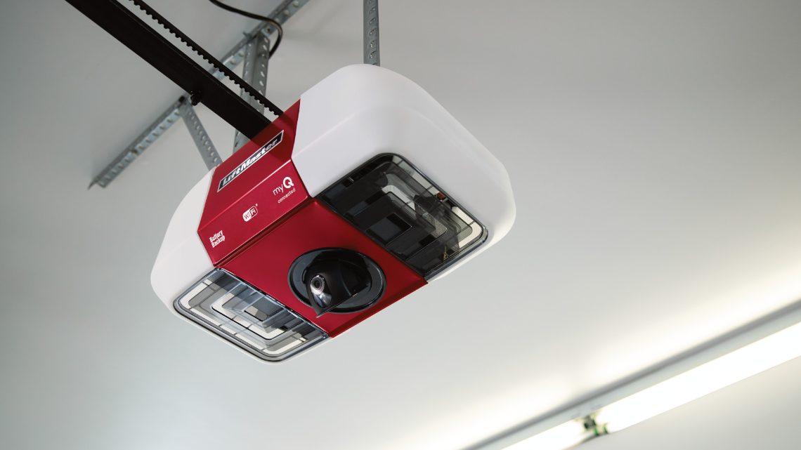 A red and white LiftMaster opener head unit mounted on a garage ceiling at the end of its rail, with a camera lens in the underside and myQ and Wi-Fi markings on the housing