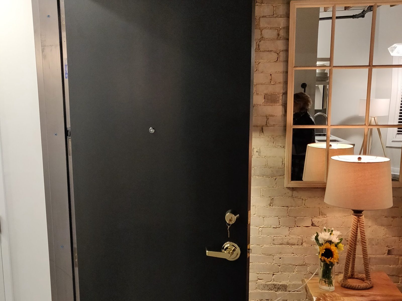 A heavy black-faced door standing open in a steel frame at a loft suite entry, with a viewer, brass cylinder and lever, installed by Canuck Door Systems