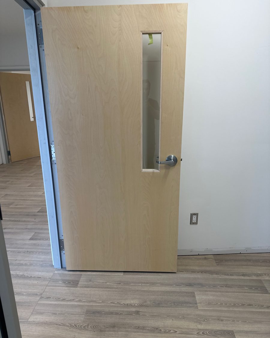 A veneer commercial door with a long stainless pull in a finished interior, installed by Canuck Door Systems