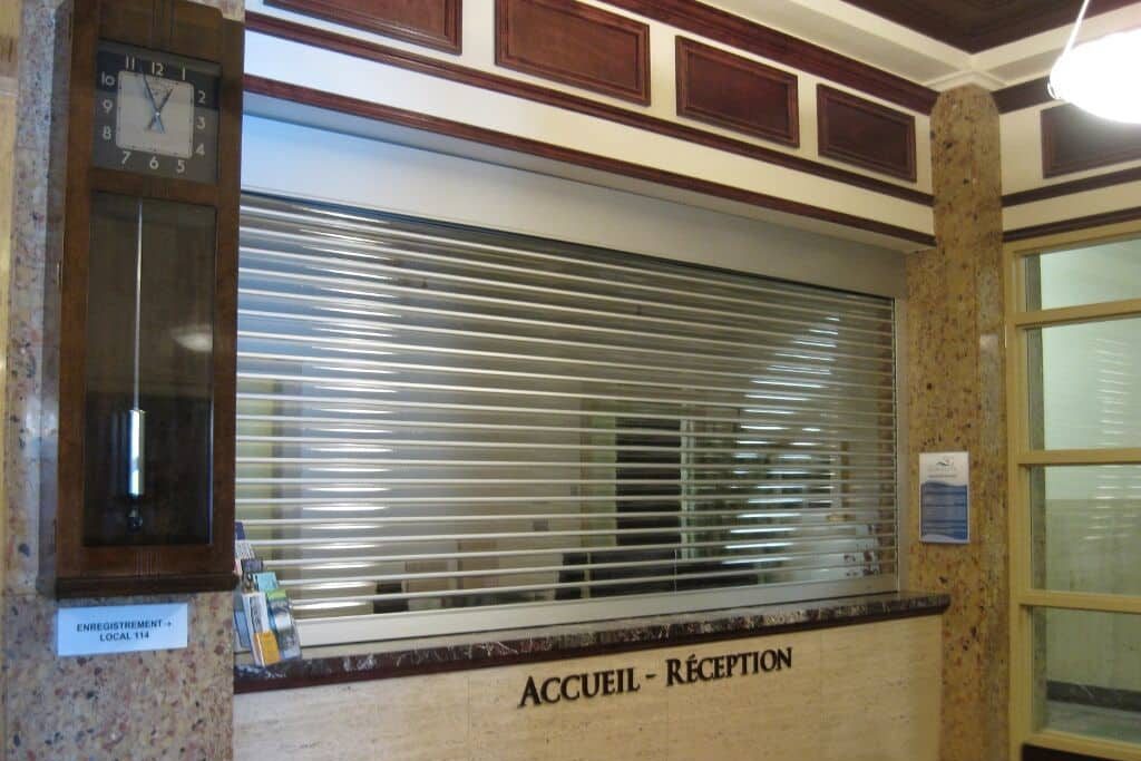 An aluminum counter shutter closed over a reception hatch in a marble-clad lobby — a Pentagon product photograph of the system we supply