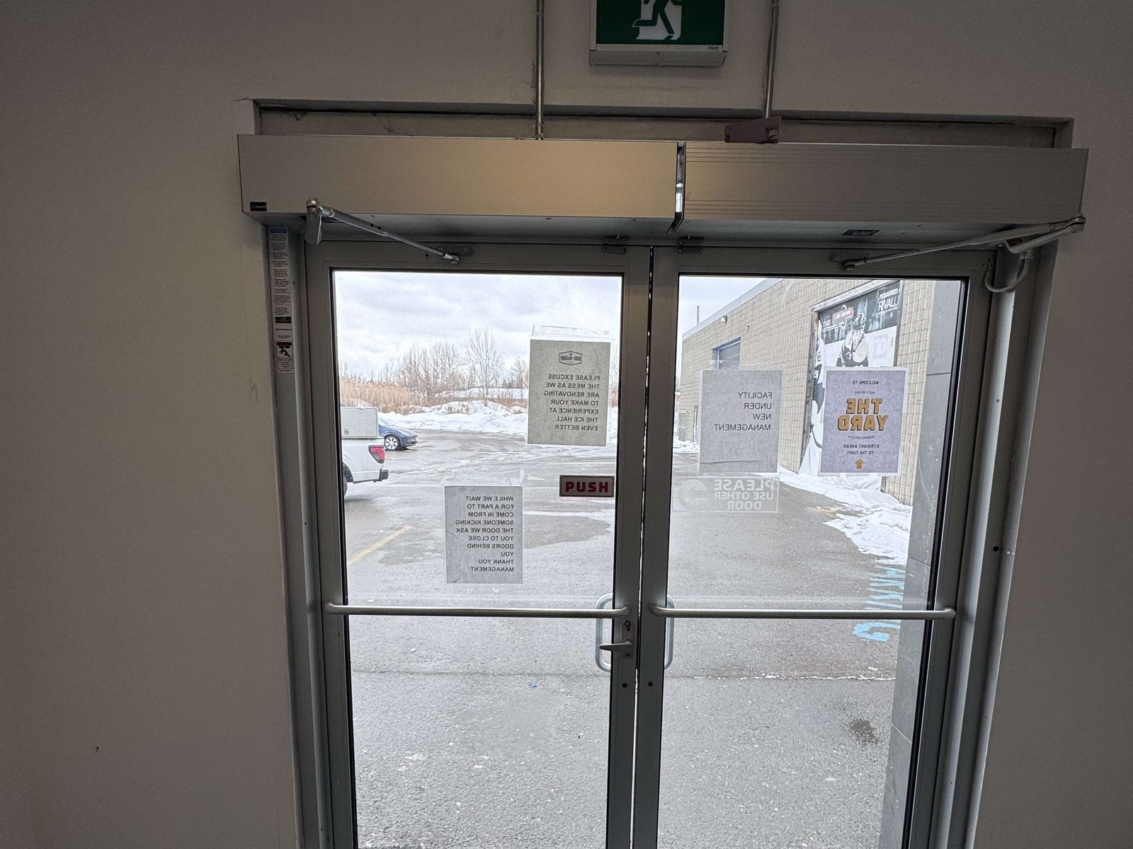 A pair of glazed entrance doors with surface-mounted automatic operators above them at a commercial building entrance in winter, serviced by Canuck Door Systems