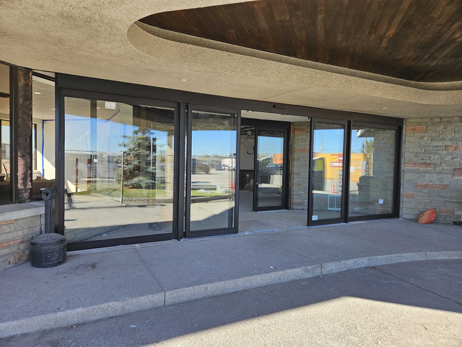 A bi-parting automatic sliding entrance in dark aluminum framing under a curved wood soffit at a Mississauga building, installed by Canuck Door Systems