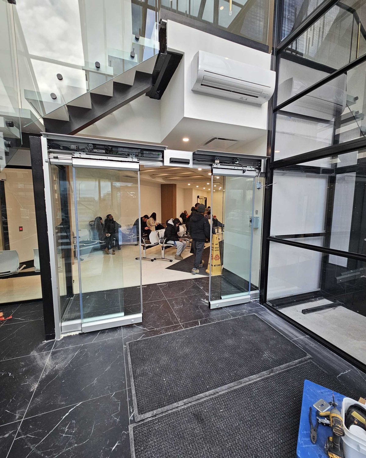 An automatic sliding glass entrance at a clinic with its operator header opened, exposing the drive, belt and controller above the doors, serviced by Canuck Door Systems