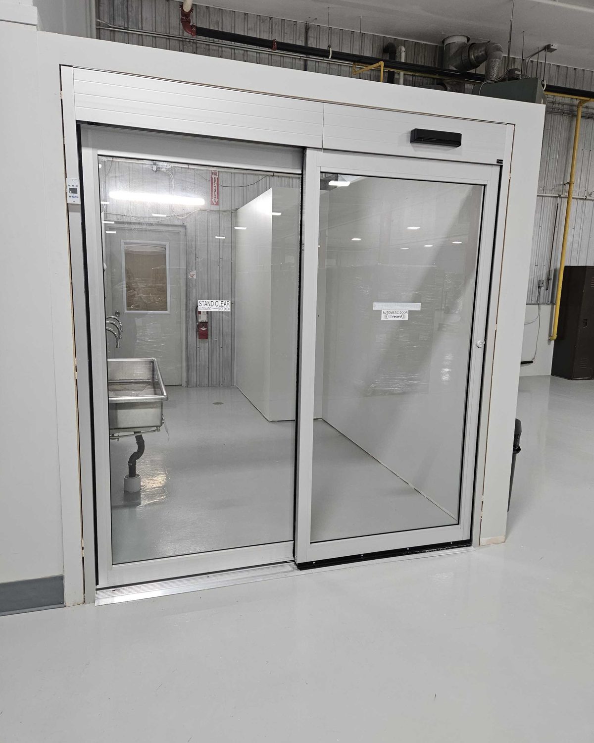 A clear-anodized automatic sliding door between production areas inside a food-processing plant, installed by Canuck Door Systems