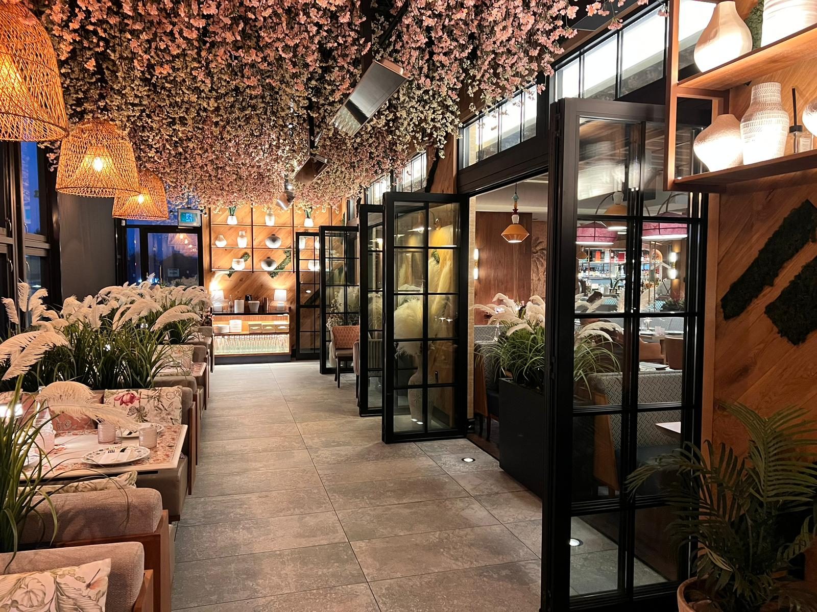 Black-framed bi-folding glass leaves running the length of a restaurant dining room, partly folded open, installed by Canuck Door Systems