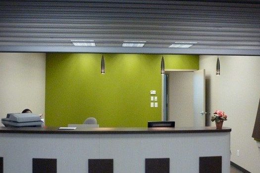 A slat counter shutter rolled up above an office reception desk, its hood and curtain spanning the full width of the opening, installed by Canuck Door Systems