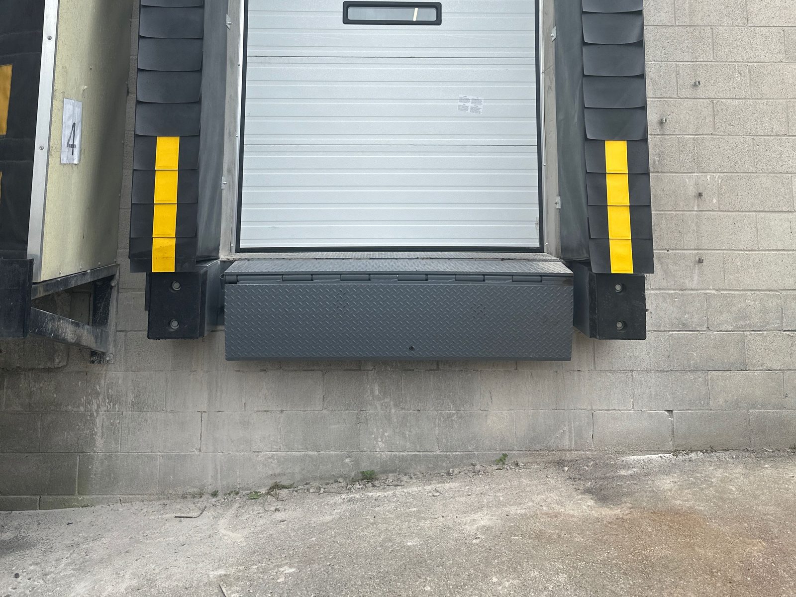Black laminated rubber dock bumpers mounted either side of a dock opening below a compression seal and diamond-plate leveler, installed by Canuck Door Systems