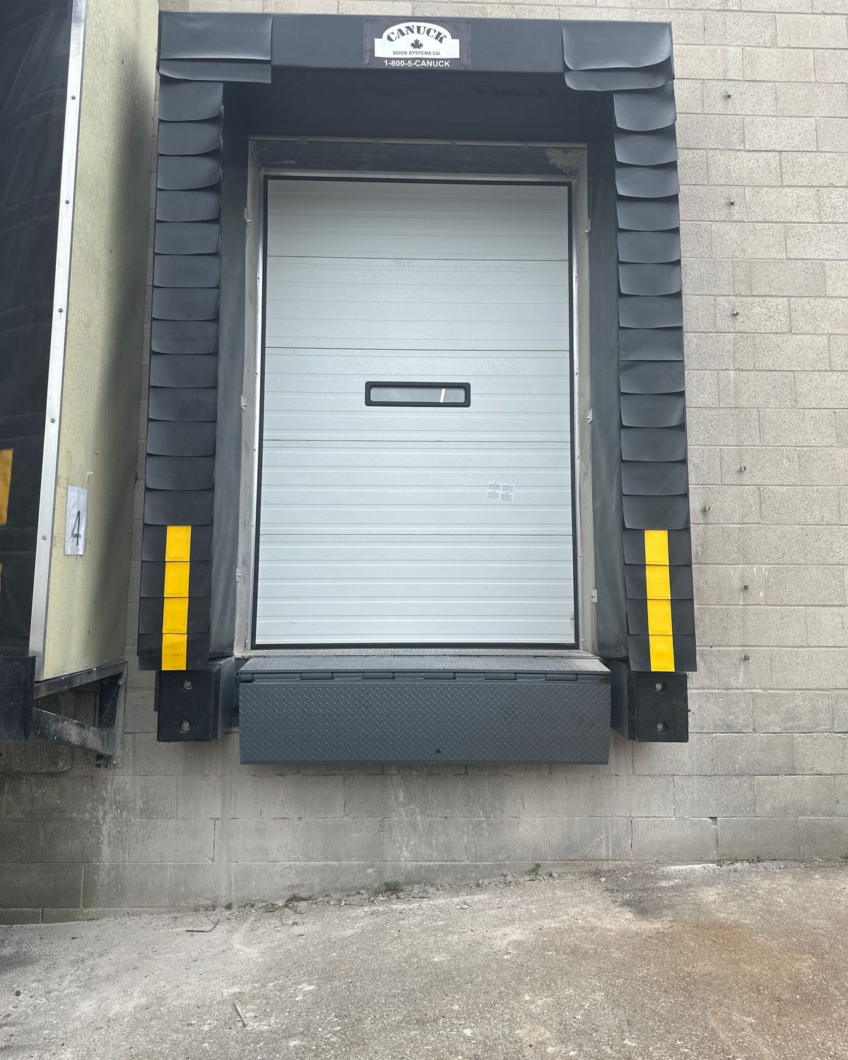 Black laminated rubber dock bumpers at the base of a dock opening with yellow-striped compression seal pads above them, installed by Canuck Door Systems
