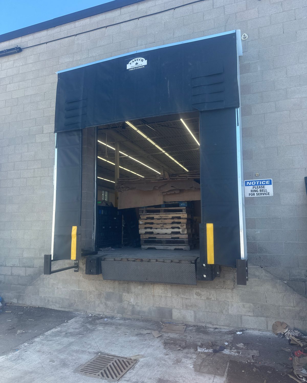 An open loading dock bay with a black fabric dock shelter, guide stripes and laminated rubber bumpers, serviced by Canuck Door Systems
