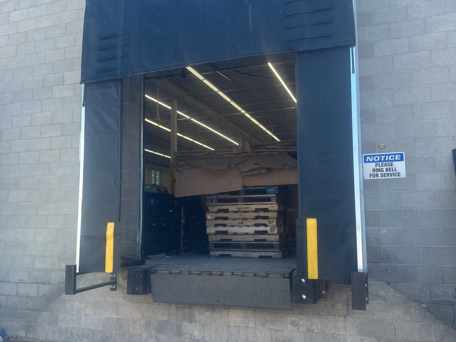 A loading dock bay fitted with a black fabric dock shelter with head and side curtains and yellow guide stripes, over an open dock opening, installed by Canuck Door Systems