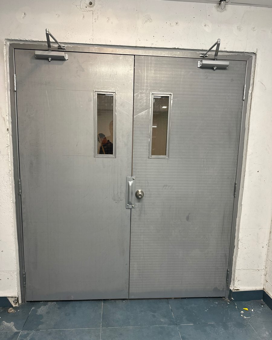 A pair of steel doors with vision lites and surface-mounted door closers on each leaf in a commercial corridor, installed by Canuck Door Systems