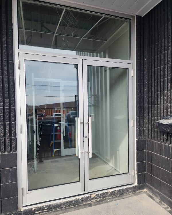 An aluminum-framed pair of commercial entrance doors with glazed sidelites in a dark brick elevation, worked on by Canuck Door Systems