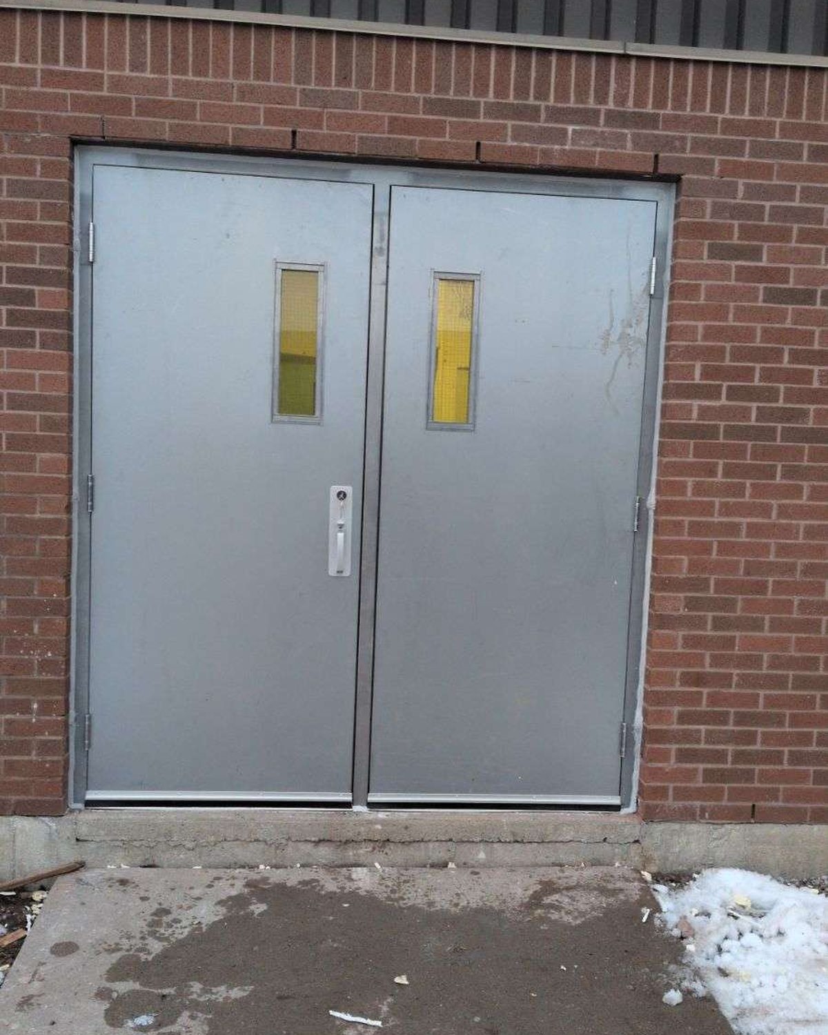 A pair of exterior steel doors in a brick wall with an astragal at the meeting stile, of the type Canuck Door Systems weatherstrips and seals