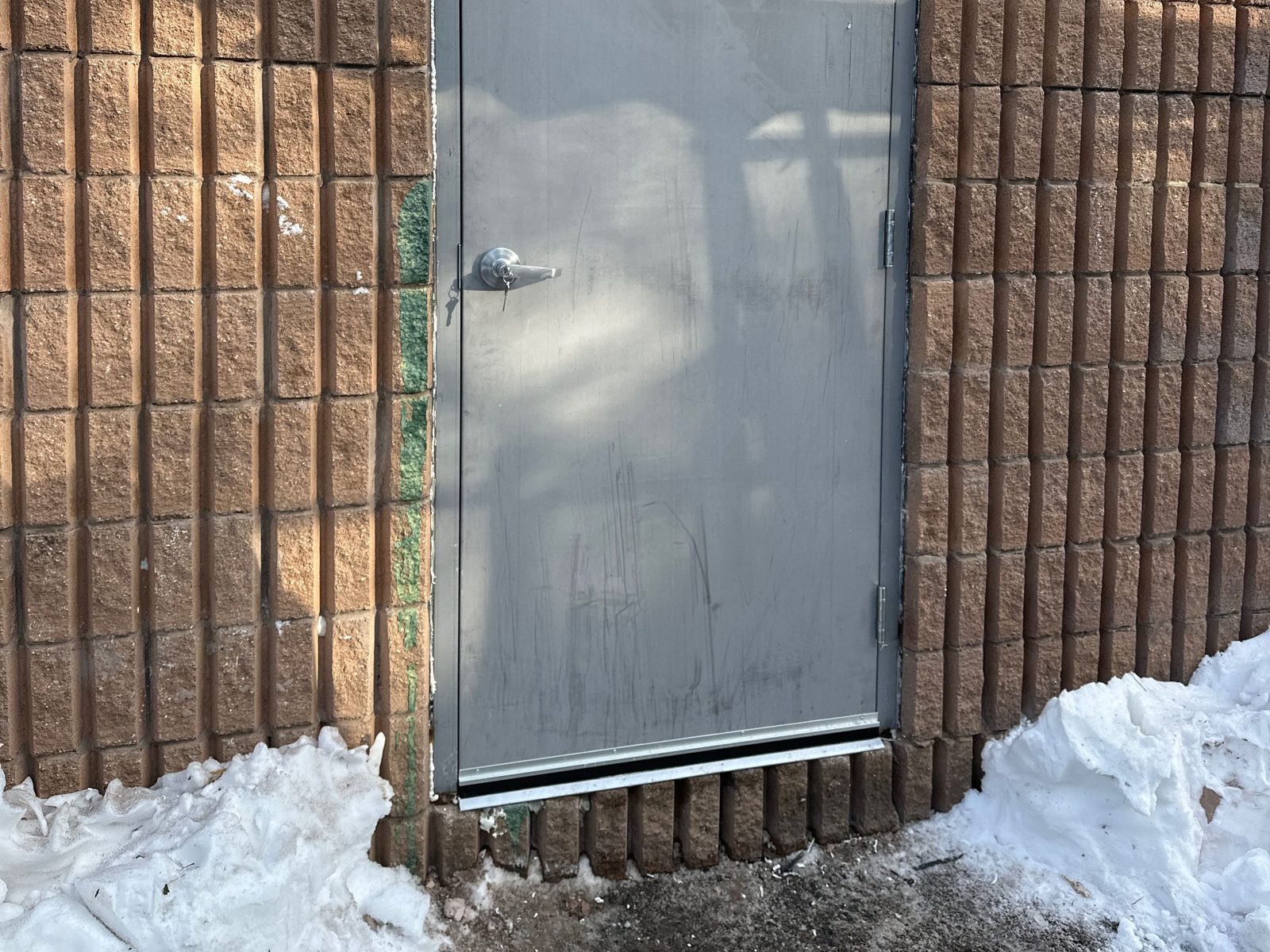 An exterior steel door in a brick wall with snow banked against the threshold, of the type Canuck Door Systems reseals and reweatherstrips