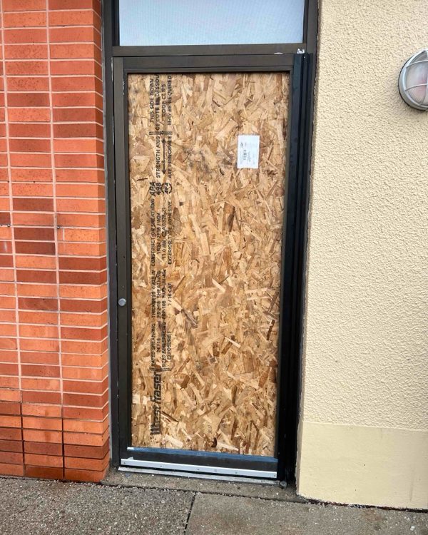 A commercial entrance door opening secured with plywood boarding fixed into the aluminum frame, by Canuck Door Systems