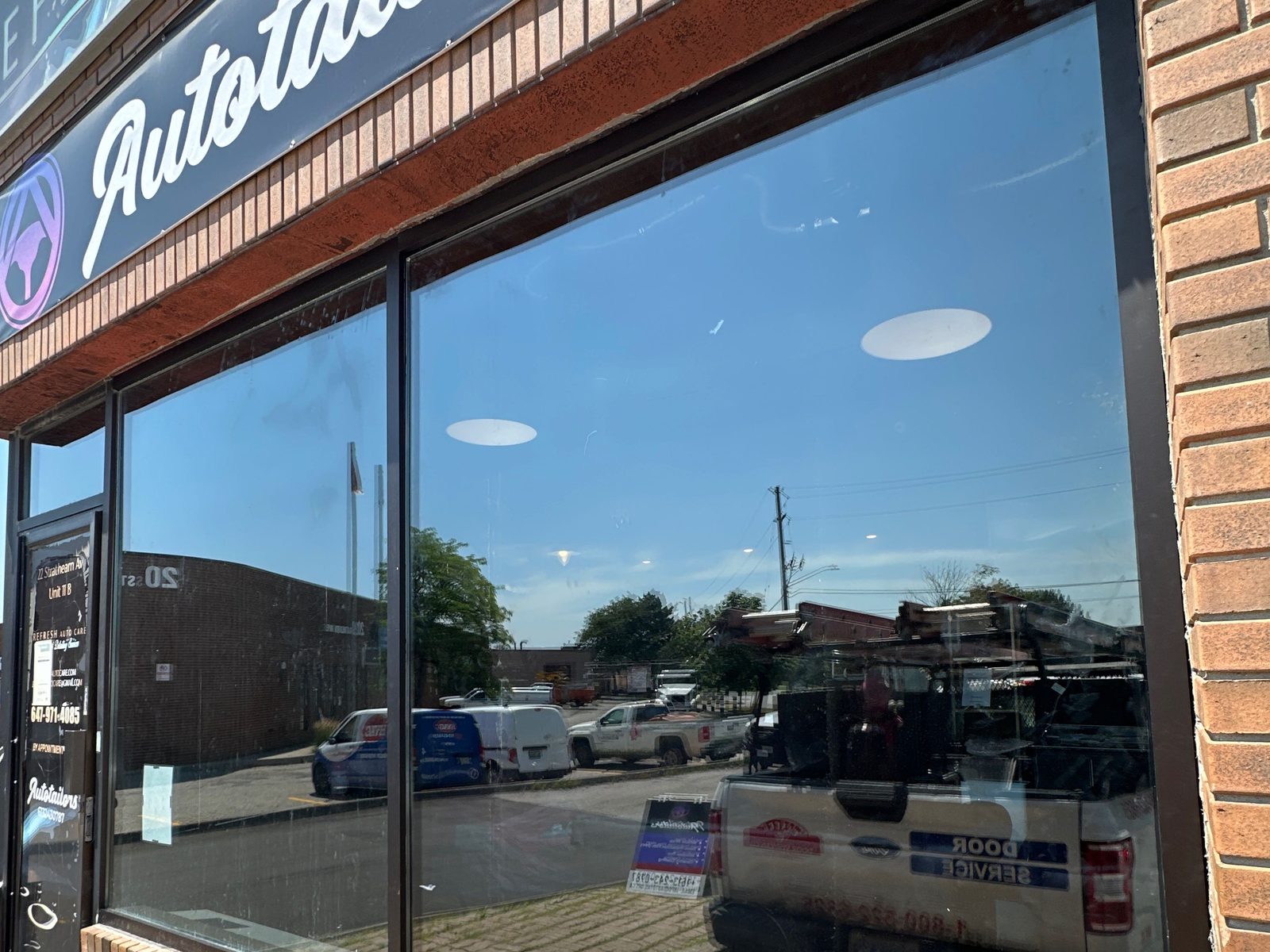 A full-width shopfront glazing bay in dark aluminum framing set into a brick storefront, reglazed by Canuck Door Systems