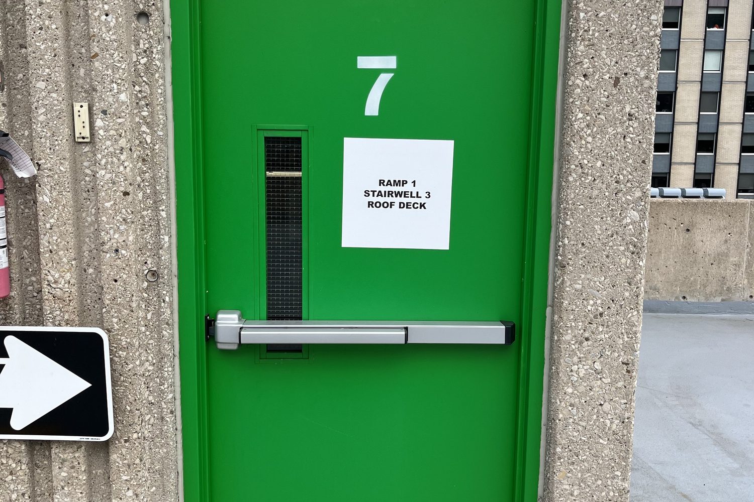 A green-painted stairwell fire door with an exit device and level number in a concrete stair lobby, inspected by Canuck Door Systems