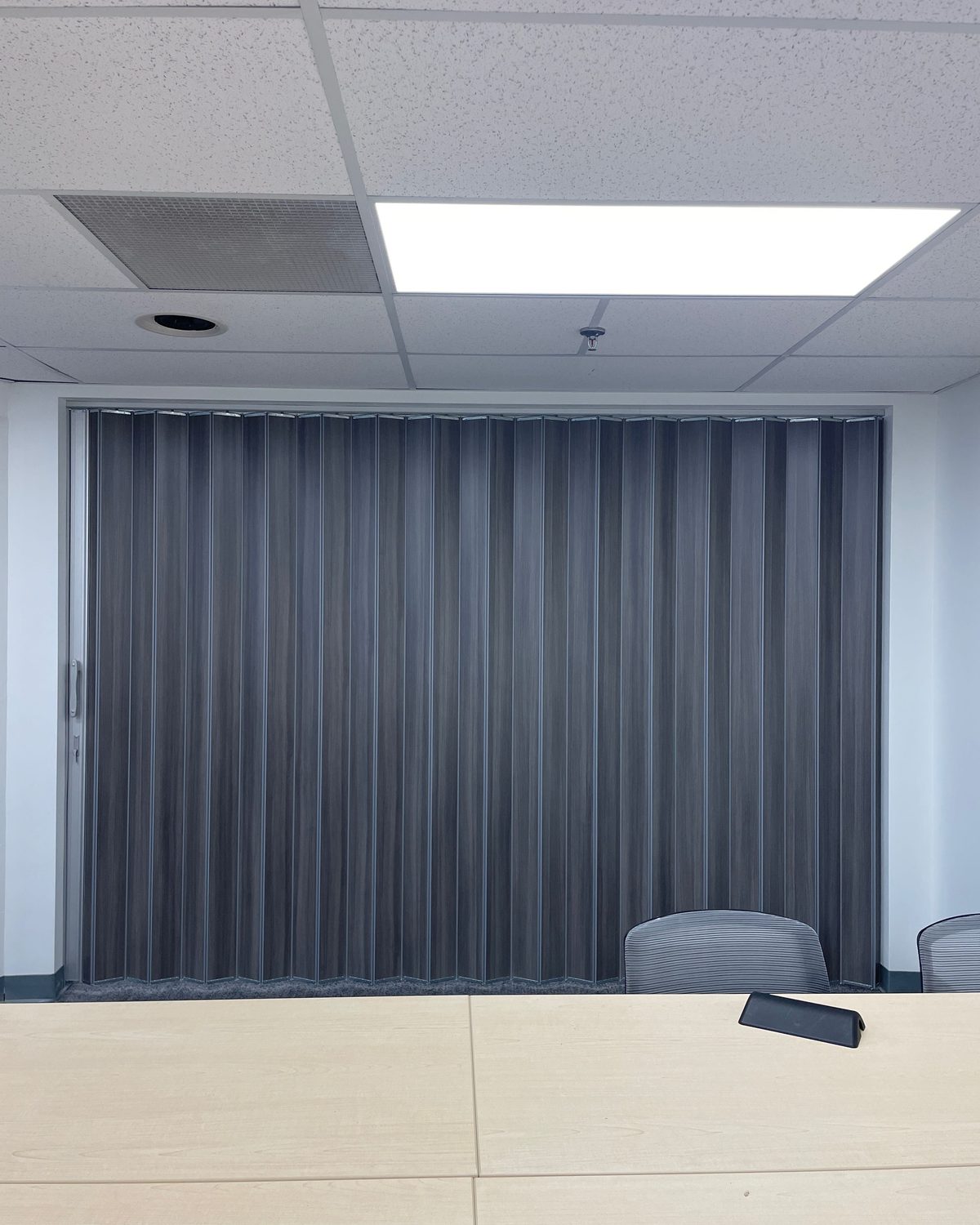 A dark grey accordion folding partition closed across the end of a meeting room, installed by Canuck Door Systems