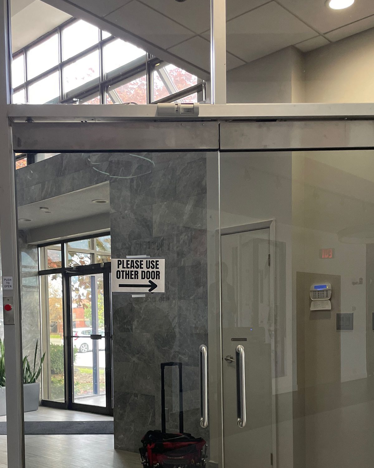 A frameless glass door pair with patch fittings and full-height glass screens in a stone-clad office lobby, installed by Canuck Door Systems