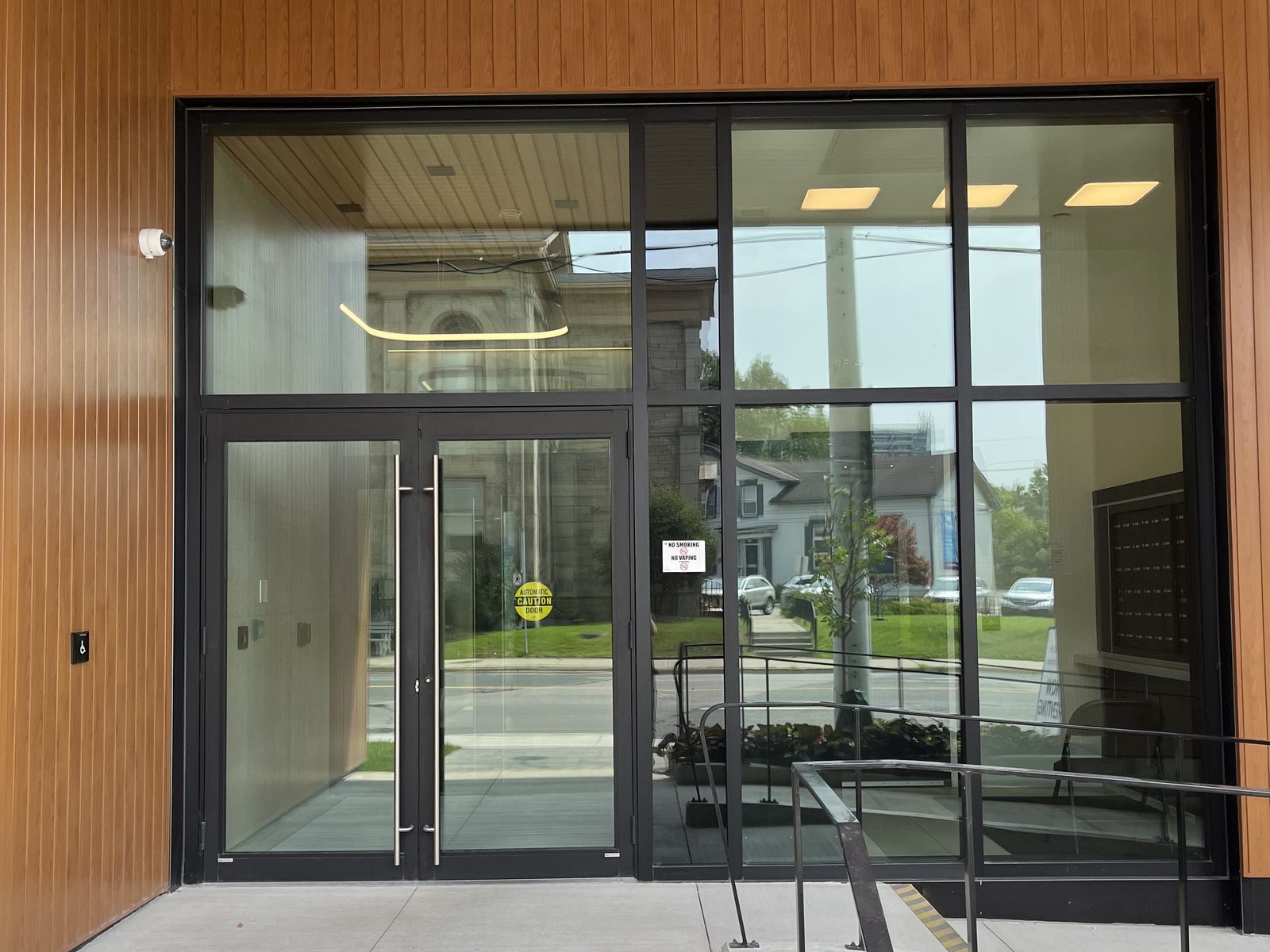 Dark aluminum entrance with a pair of narrow-stile glass doors on automatic operators, sidelites and a full-height glazed screen set into a wood-clad elevation, supplied and installed by Canuck Door Systems