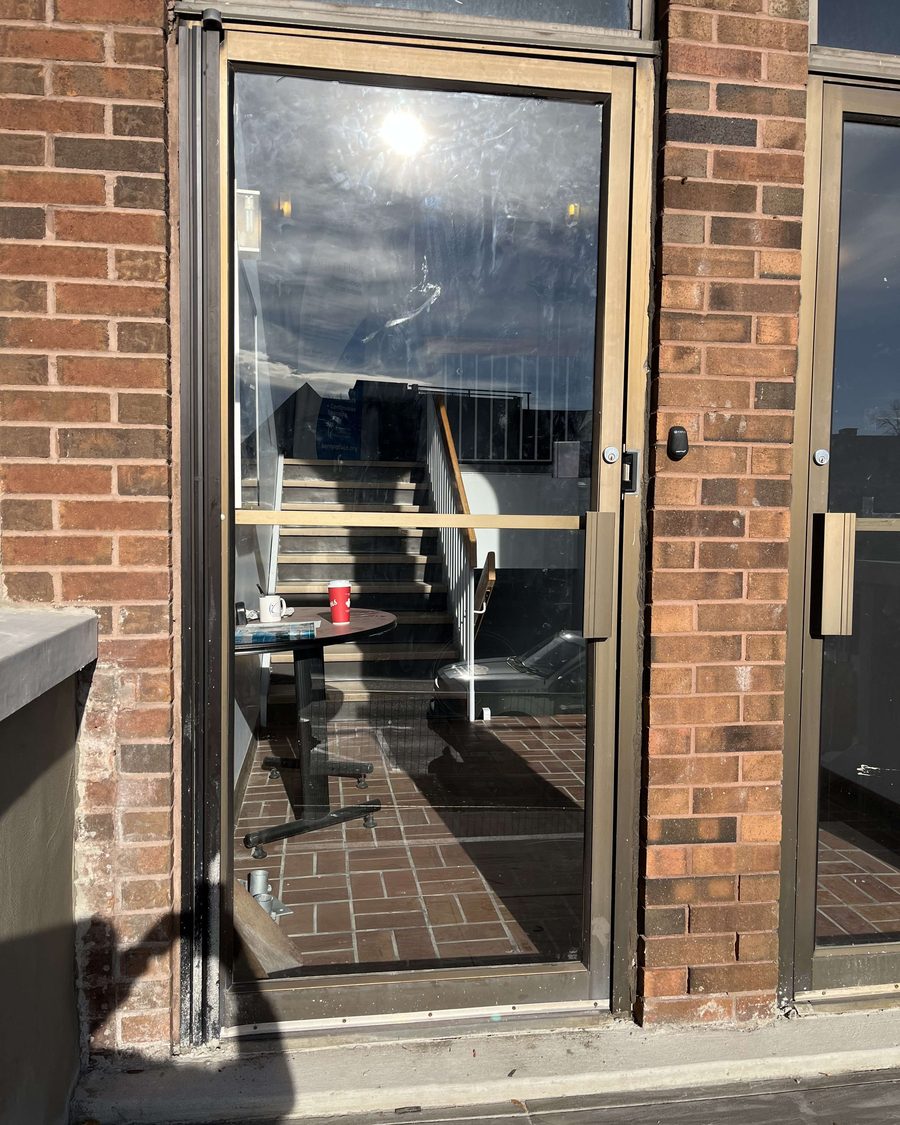 A dark aluminum glass entrance door with a full-height sidelite set into a brick opening, glazed by Canuck Door Systems