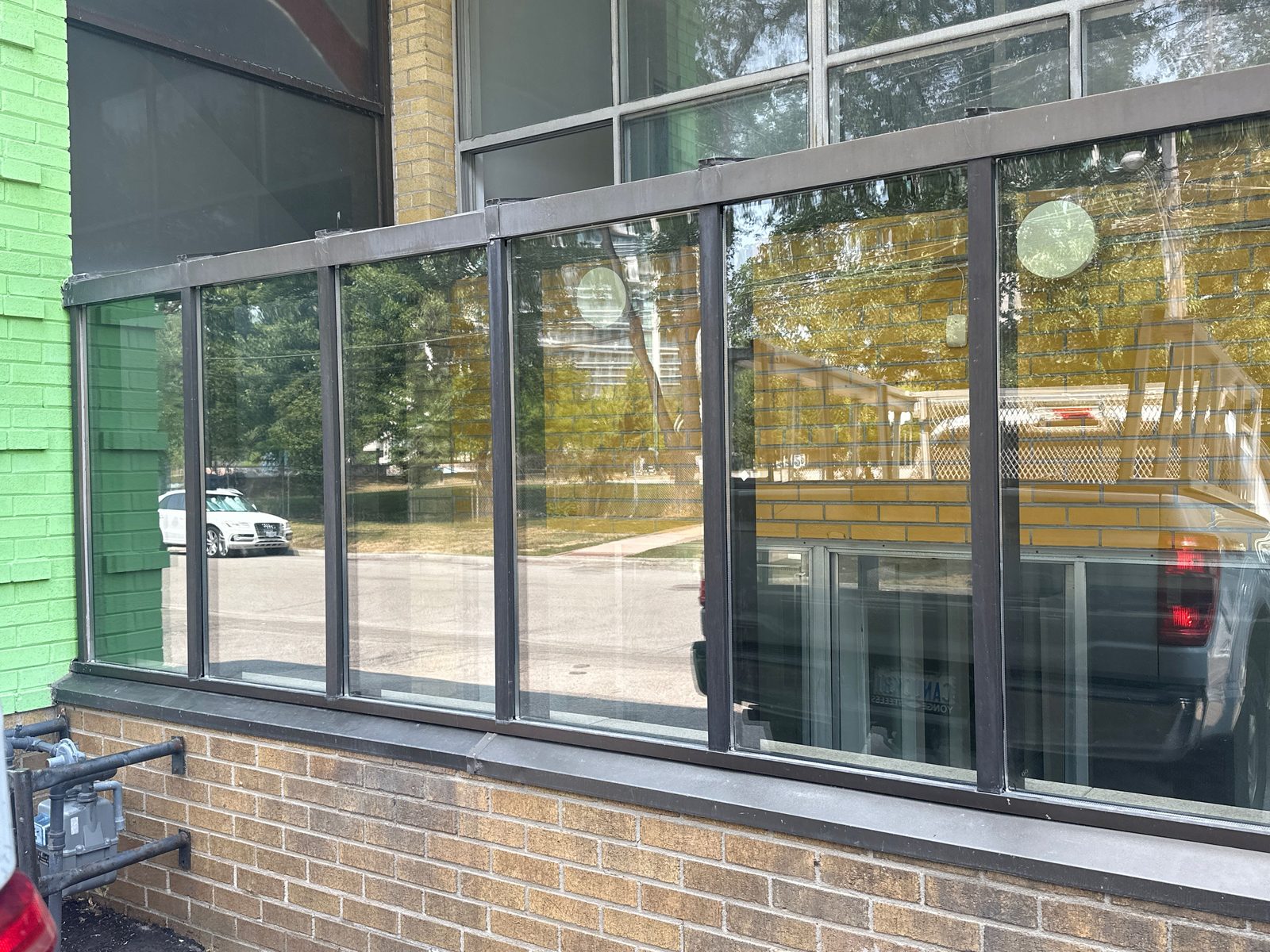Run of aluminum-framed commercial windows on a brick elevation being reglazed, with glazing equipment set up below, by Canuck Door Systems