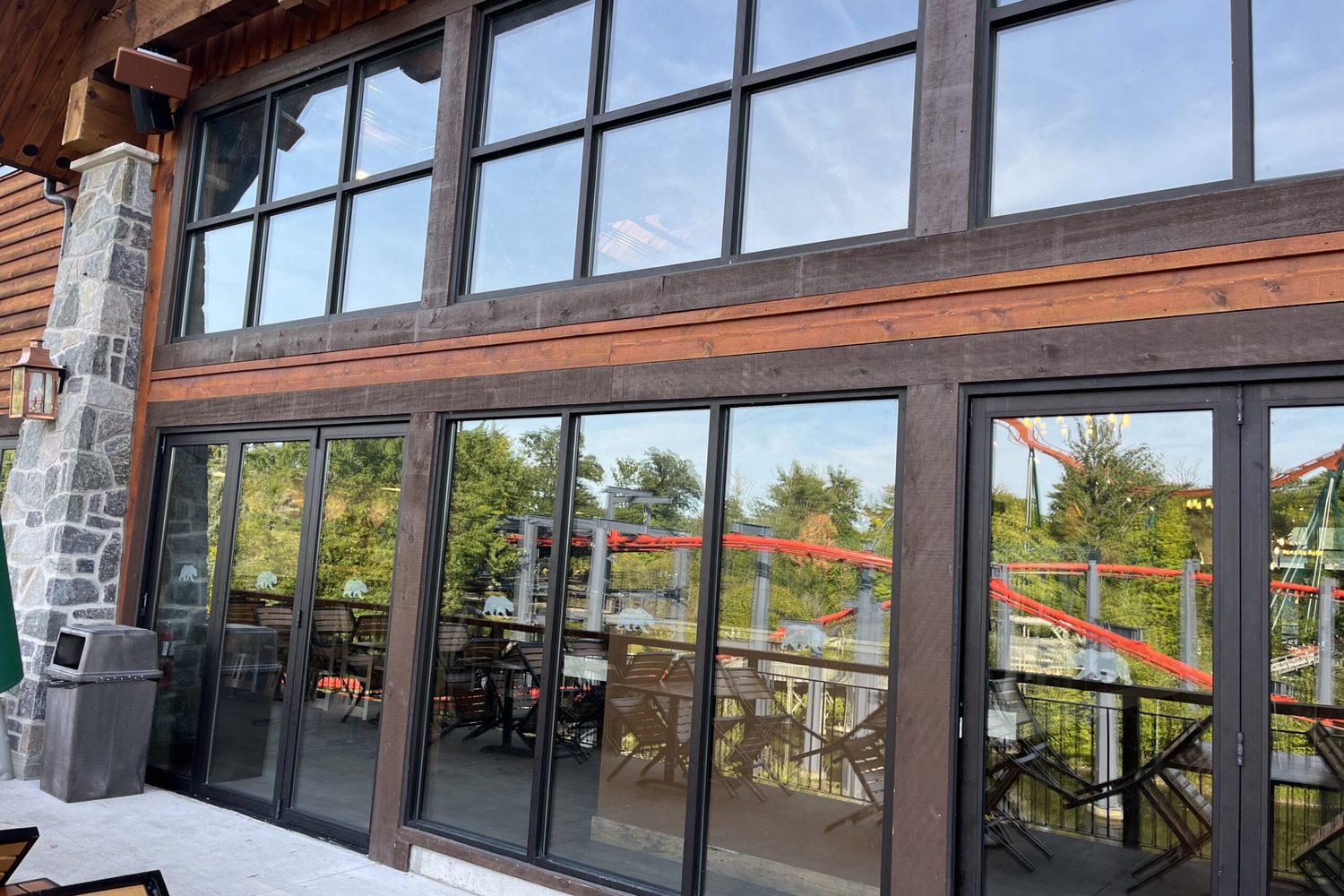 A dark-framed glazed screen with sliding glass doors and a transom above, set into the timber structure of a restaurant patio, installed by Canuck Door Systems
