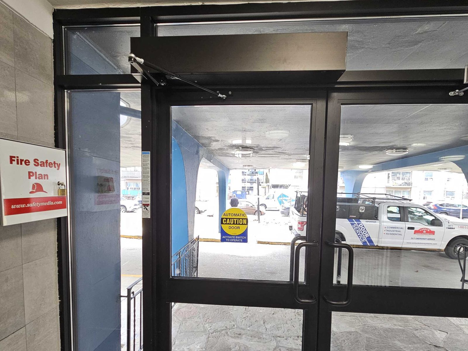An aluminum glazed entrance with a surface-mounted low-energy door operator above the leaves and a push plate at the vestibule, installed by Canuck Door Systems