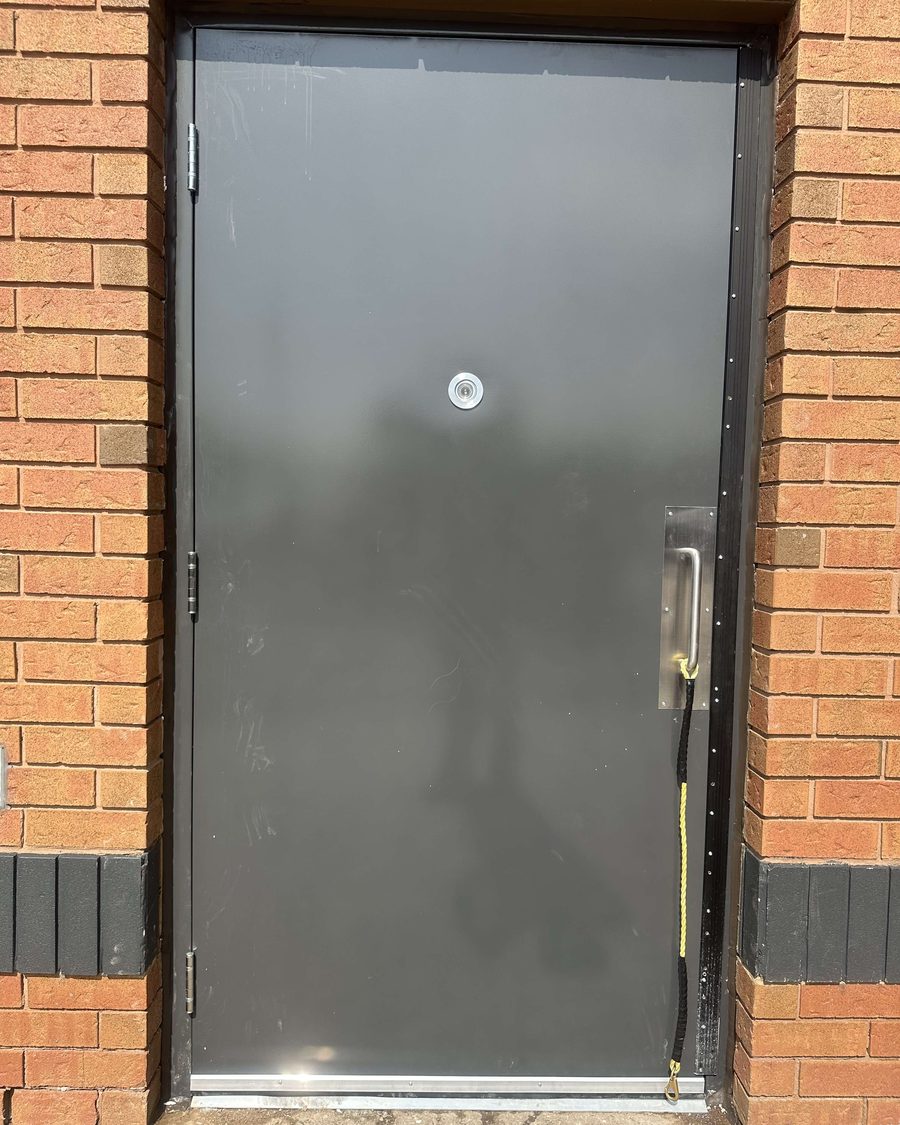 A painted hollow metal service door with a door viewer and pull handle, hung in a steel frame in a brick opening, installed by Canuck Door Systems