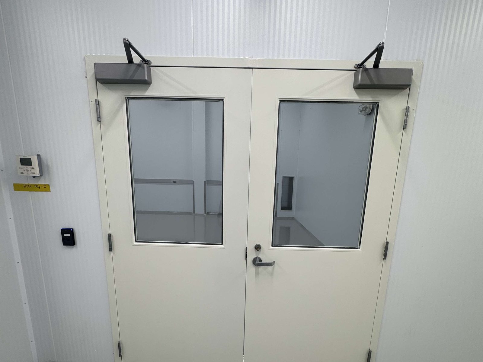 A pair of painted hollow metal doors with large vision lites and surface-mounted closers in a clean-room wall, installed by Canuck Door Systems