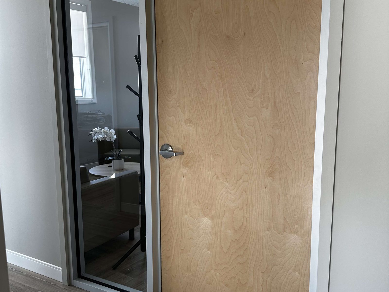 A light veneer door with a full-height vision panel beside it in a finished clinic corridor, installed by Canuck Door Systems