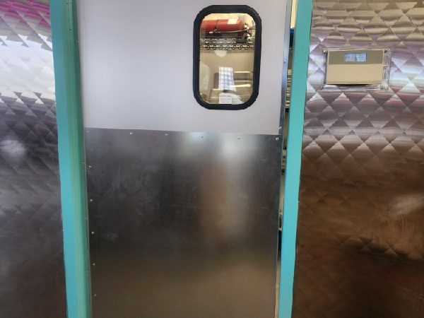 A commercial kitchen traffic door with a vision window and stainless steel lower panel in a teal-painted frame, installed by Canuck Door Systems