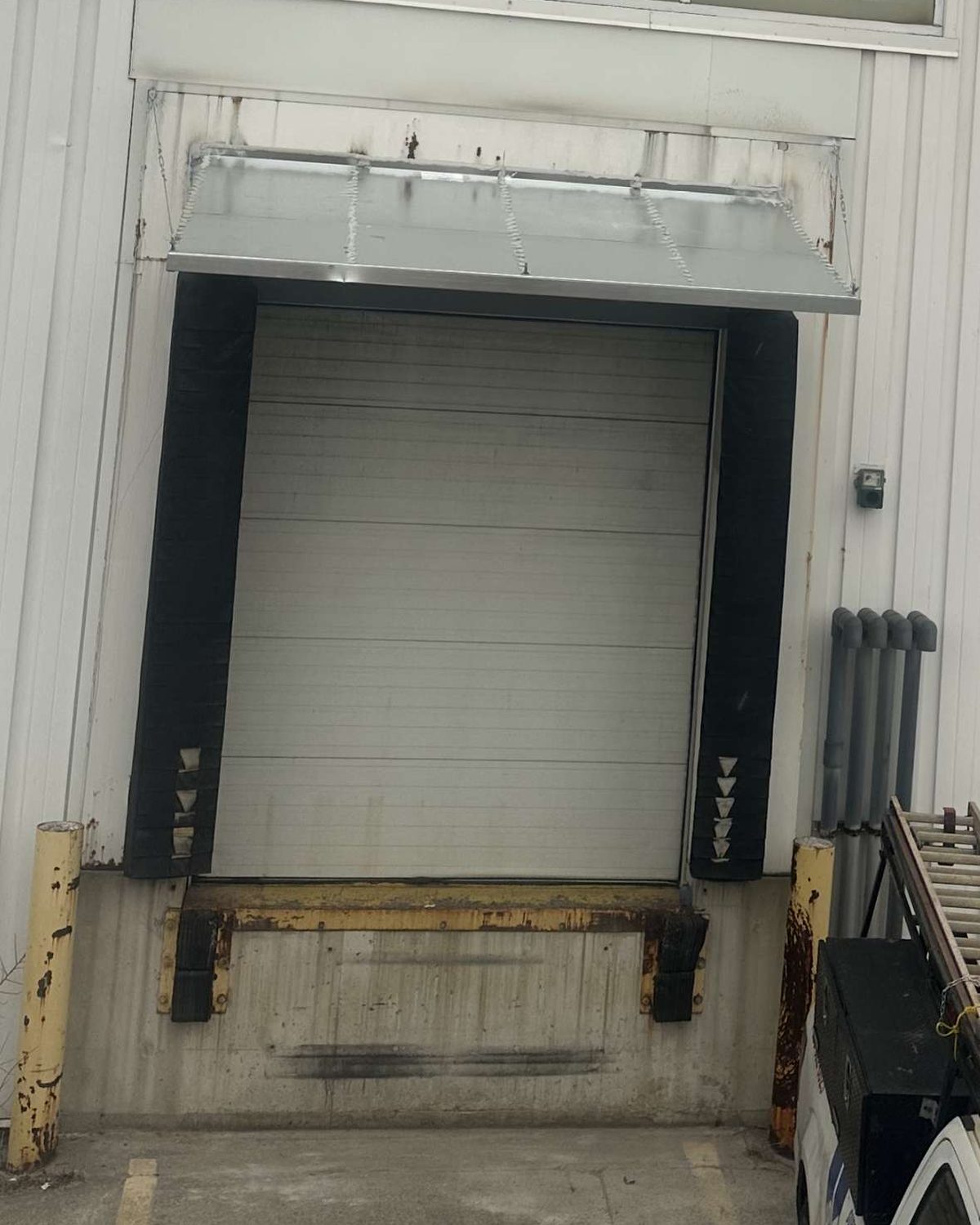 A dock position with black compression seal pads, a galvanized head canopy and an older leveler frame showing corrosion, photographed on a service visit by Canuck Door Systems