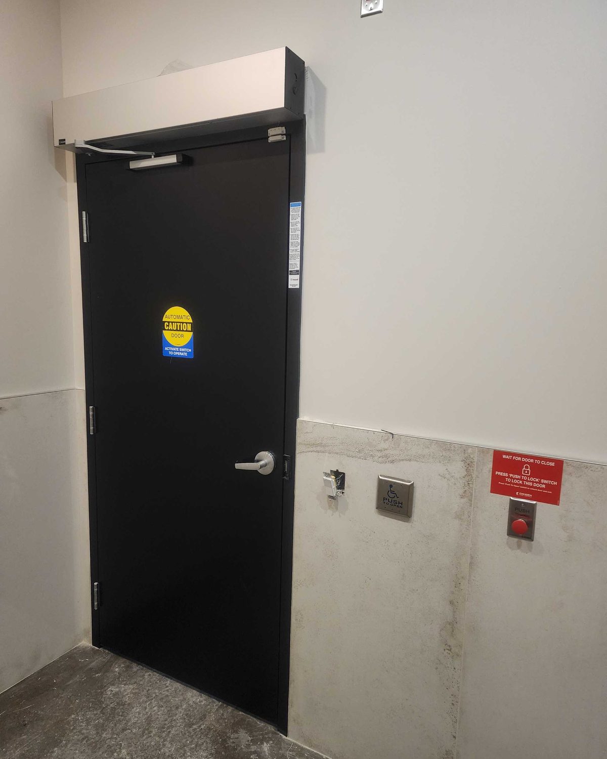A grey hollow metal door in a painted steel frame in a block-wall back-of-house room, installed by Canuck Door Systems