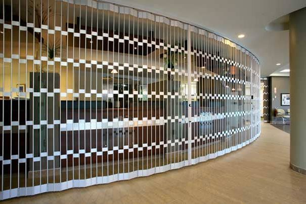 An open-style folding security grille closed across a curved lobby run inside a building, installed by Canuck Door Systems