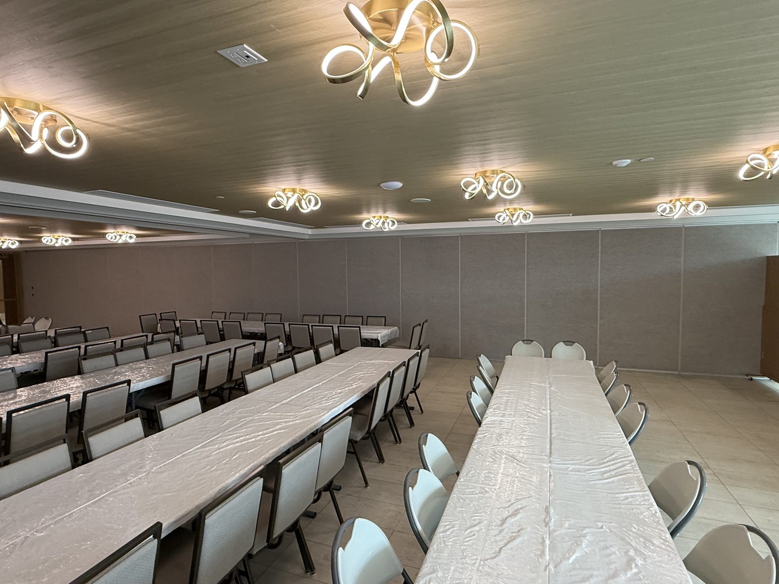 A fabric-faced operable partition wall running down one side of a banquet hall set with long tables and chairs, installed by Canuck Door Systems