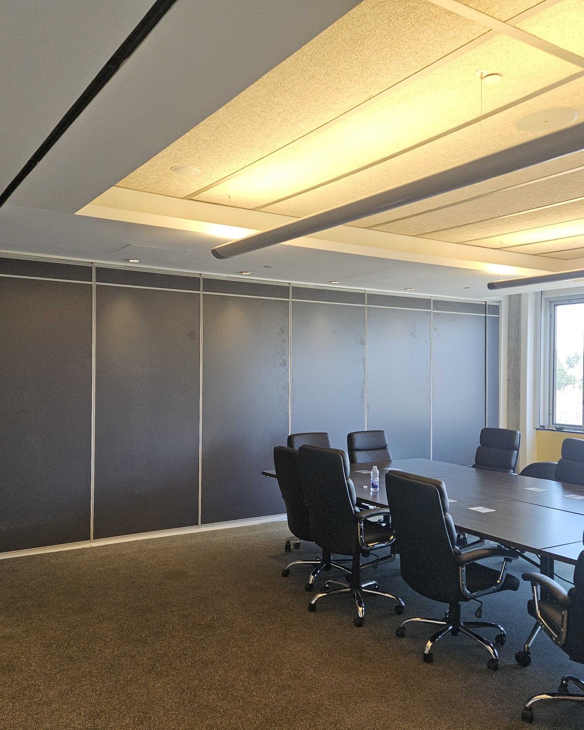 A dark panelled operable partition closed along one side of a boardroom set with a conference table and chairs, installed by Canuck Door Systems