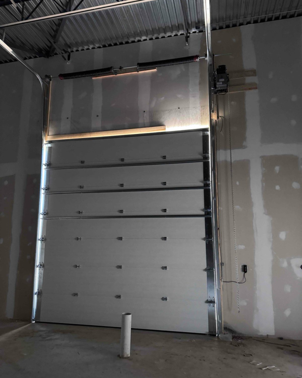 The same overhead door seen from inside: torsion spring above the opening, vertical and horizontal track, a jackshaft operator on the jamb with its chain and control station, installed by Canuck Door Systems