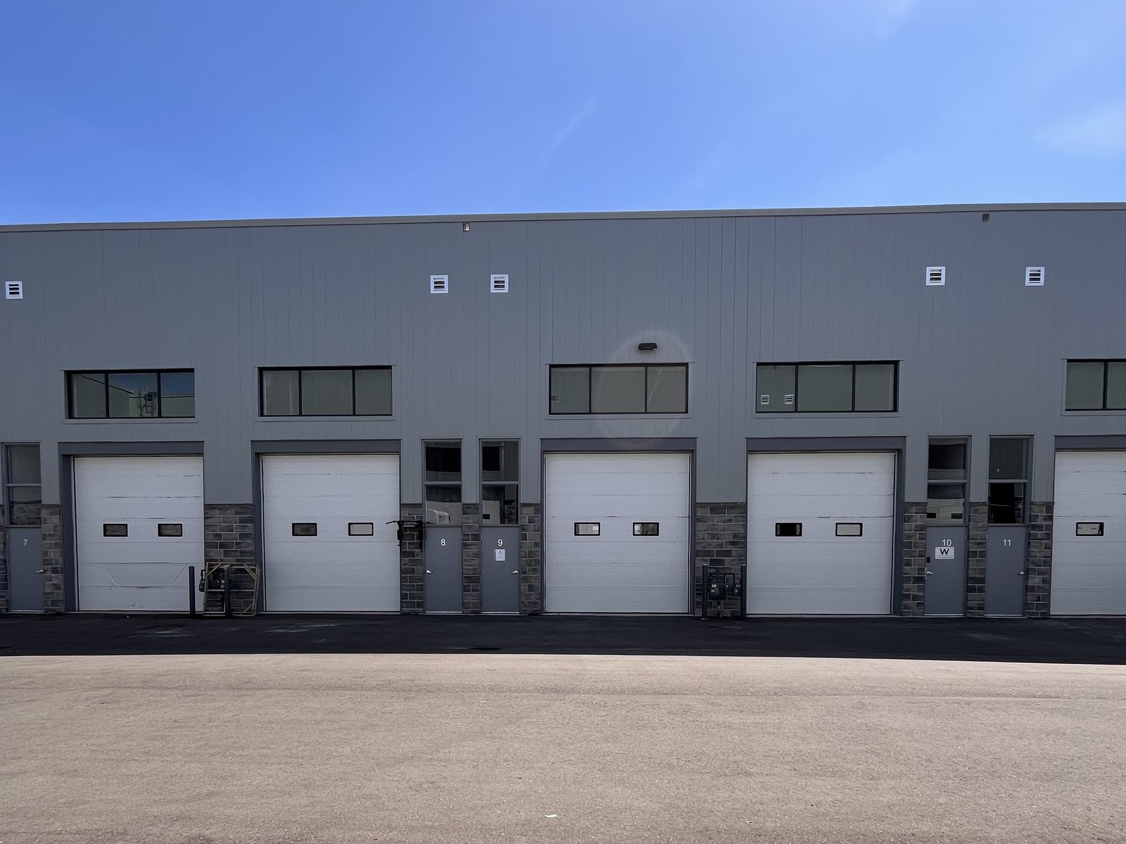 A run of white sectional overhead doors along a multi-unit industrial building under a clear sky, installed by Canuck Door Systems