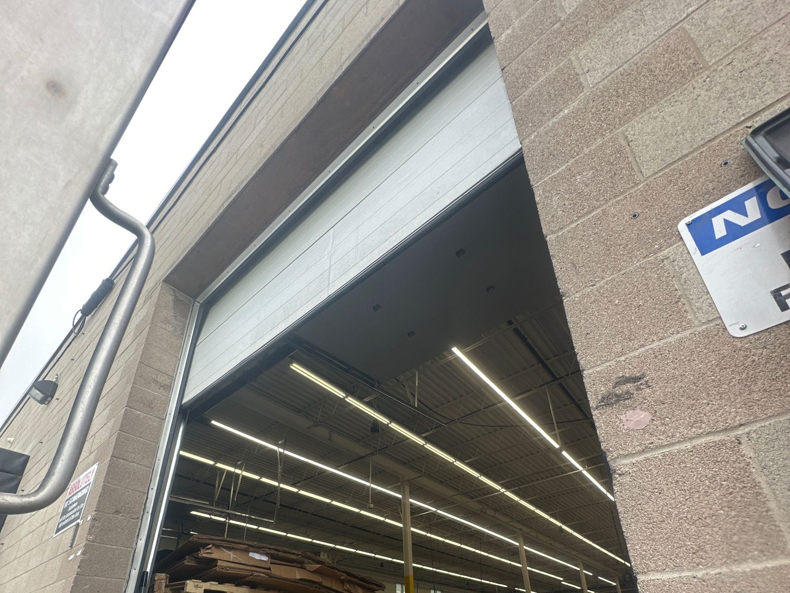 A sectional overhead door raised into its open position above a warehouse bay, the panels stacked flat under the ceiling, repaired by Canuck Door Systems