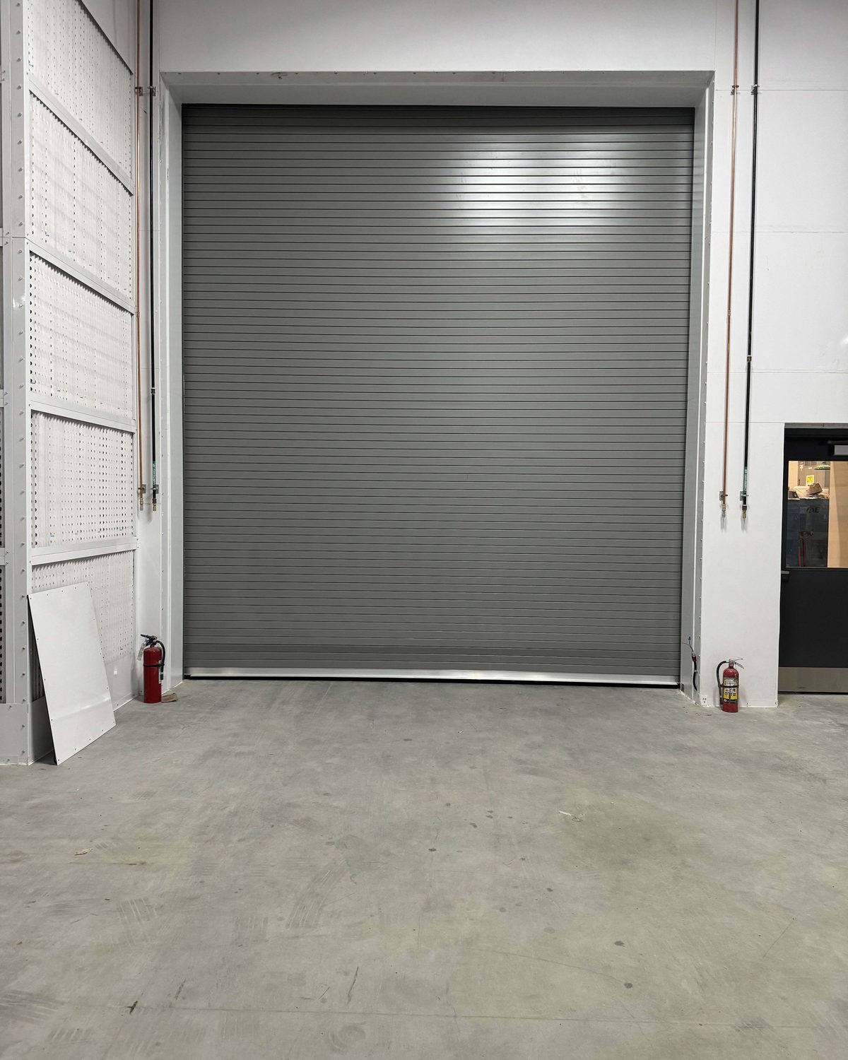 An industrial roll-up door curtain of interlocking galvanized slats inside a commercial building, installed by Canuck Door Systems