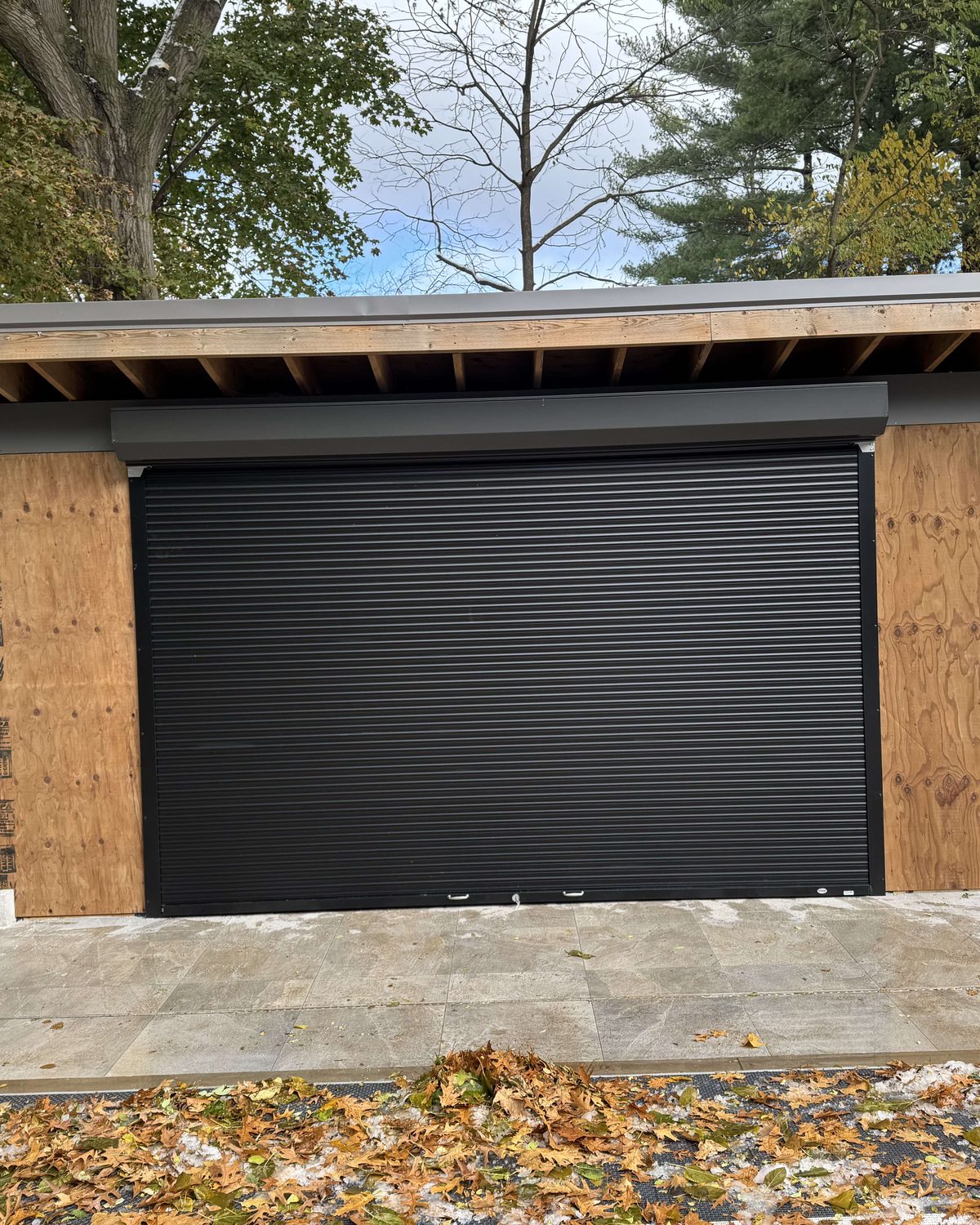 A black slat rolling shutter closed across an exterior opening, installed by Canuck Door Systems