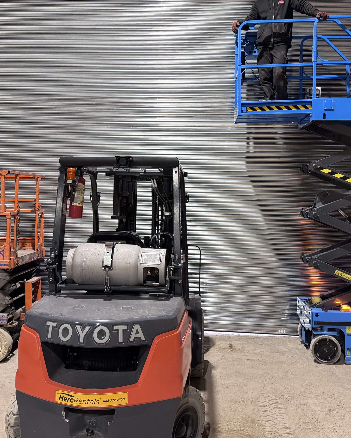 Canuck Door Systems technicians installing a galvanized rolling steel door from a scissor lift inside an industrial building