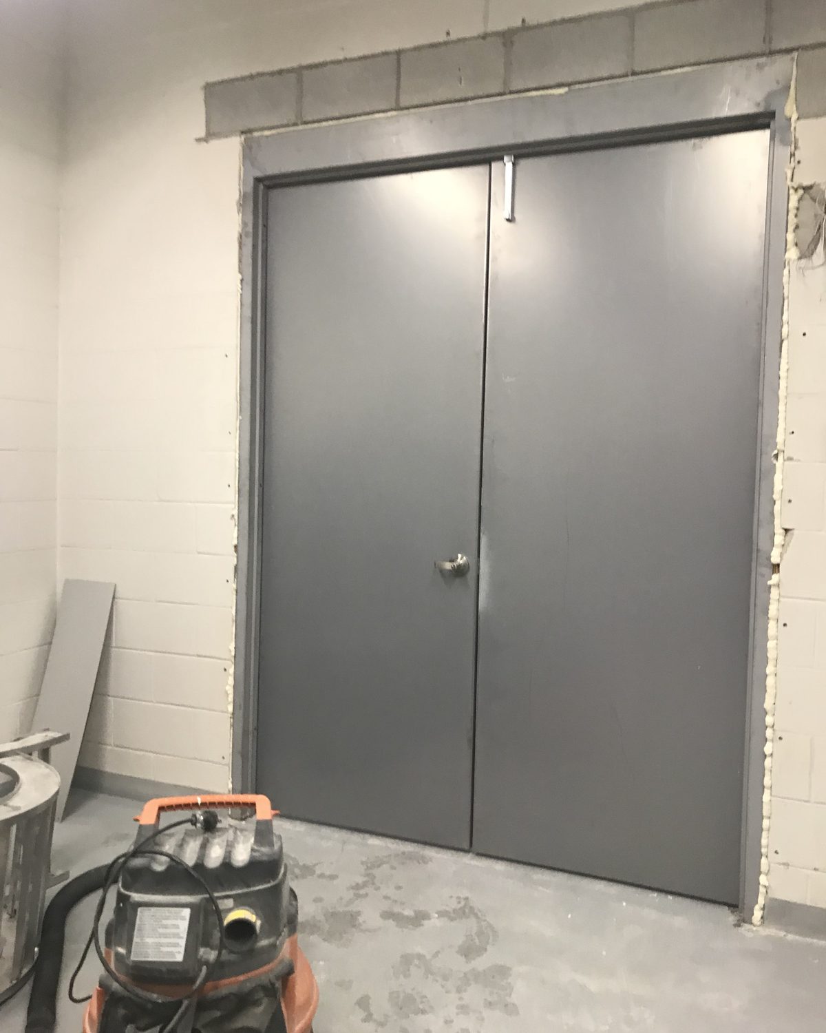 A pair of hollow metal doors in a newly set steel frame in a block wall, with foam still visible at the jamb, installed by Canuck Door Systems