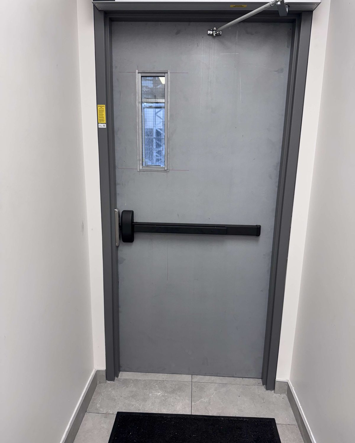 A painted hollow metal door with an exit device, closer and vision lite in a finished interior corridor, installed by Canuck Door Systems